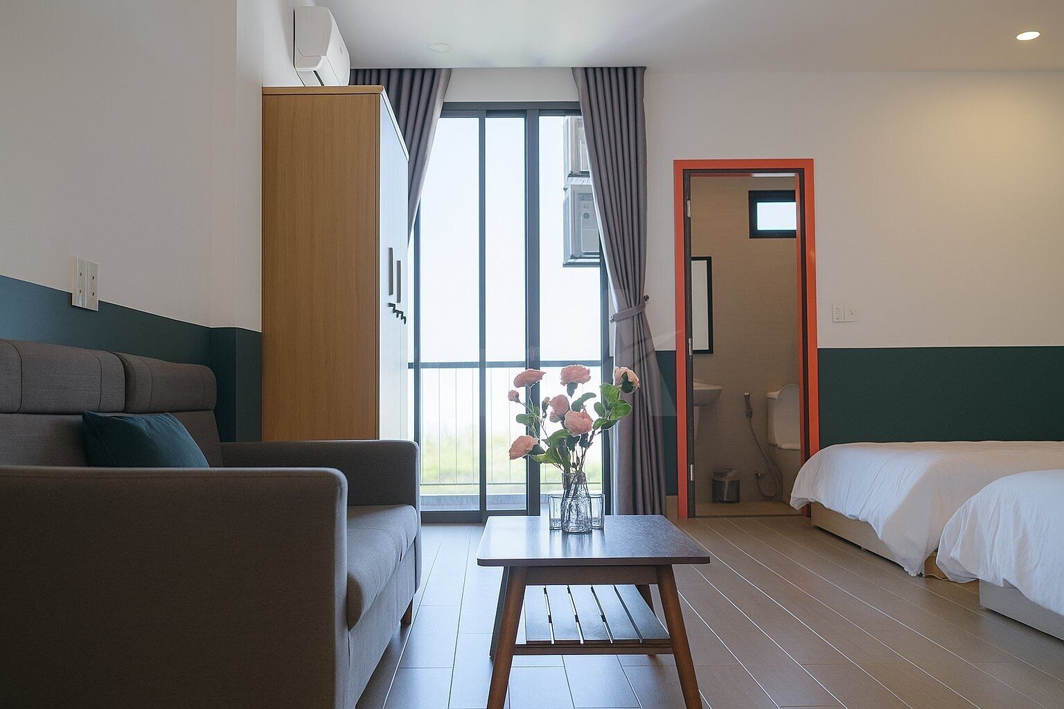 Una habitación de hotel con sofá, una mesita con un florero, cama y baño visible a través de una puerta abierta.
