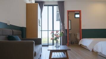 Una habitación de hotel con sofá, una mesita con un florero, cama y baño visible a través de una puerta abierta.