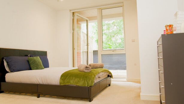 A bedroom with a bed, a wardrobe, and a window with a view of greenery. - Stylish 3BR | 3 Min to Southfields Station (Greater London)