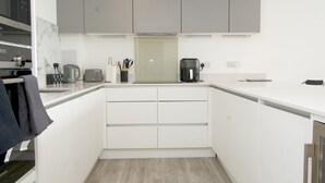 A modern kitchen with white cabinetry, a built-in oven, a coffee maker, and a toaster. - Stylish 3BR | 3 Min to Southfields Station (Greater London)