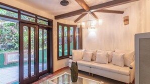 A spacious living room with a white sofa, a glass coffee table, and a view of a garden through large sliding glass doors. - House w/ 3 Suites 400m From Mucuge Beach Mcg0006 (Porto Seguro)