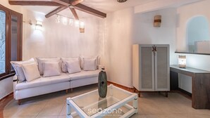 A modern living room with a glass coffee table, a white sofa, wooden beams on the ceiling, and a cabinet with a clock. - House w/ 3 Suites 400m From Mucuge Beach Mcg0006 (Porto Seguro)