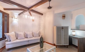 Ein modernes Wohnzimmer mit einem Glastisch, einem weißen Sofa, Holzbalken an der Decke und einem Schrank mit einer Uhr.