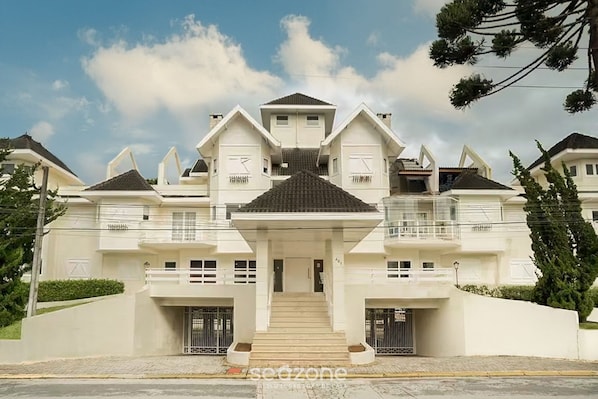 A large, modern two-story house with a symmetrical design, featuring a central staircase, multiple balconies, and a well-maintained front yard.