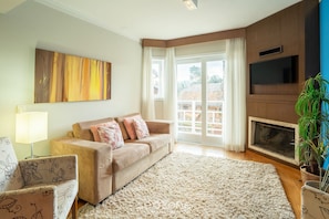 A living room with a beige sofa, a floral armchair, a large abstract painting, a flat-screen TV, and a fireplace.