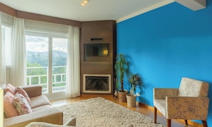 Sala de estar com lareira, um sofá, uma poltrona e vista para o exterior.
