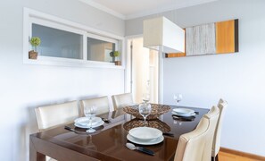 A dining area with a brown table, white chairs, and a large window. - Great apt for Families in Campos do Jordao Lvr010 (Campos do Jordão)