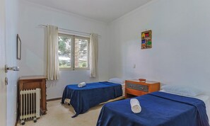 A room with two beds, a radiator, a window with curtains, and a small wooden table. - Apart w Beautiful View in Campos do Jordao Lvr0003 (Campos do Jordão)