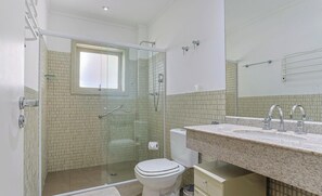 Un baño con ducha envuelta en vidrio, inodoro y lavamanos con encimera de granito.