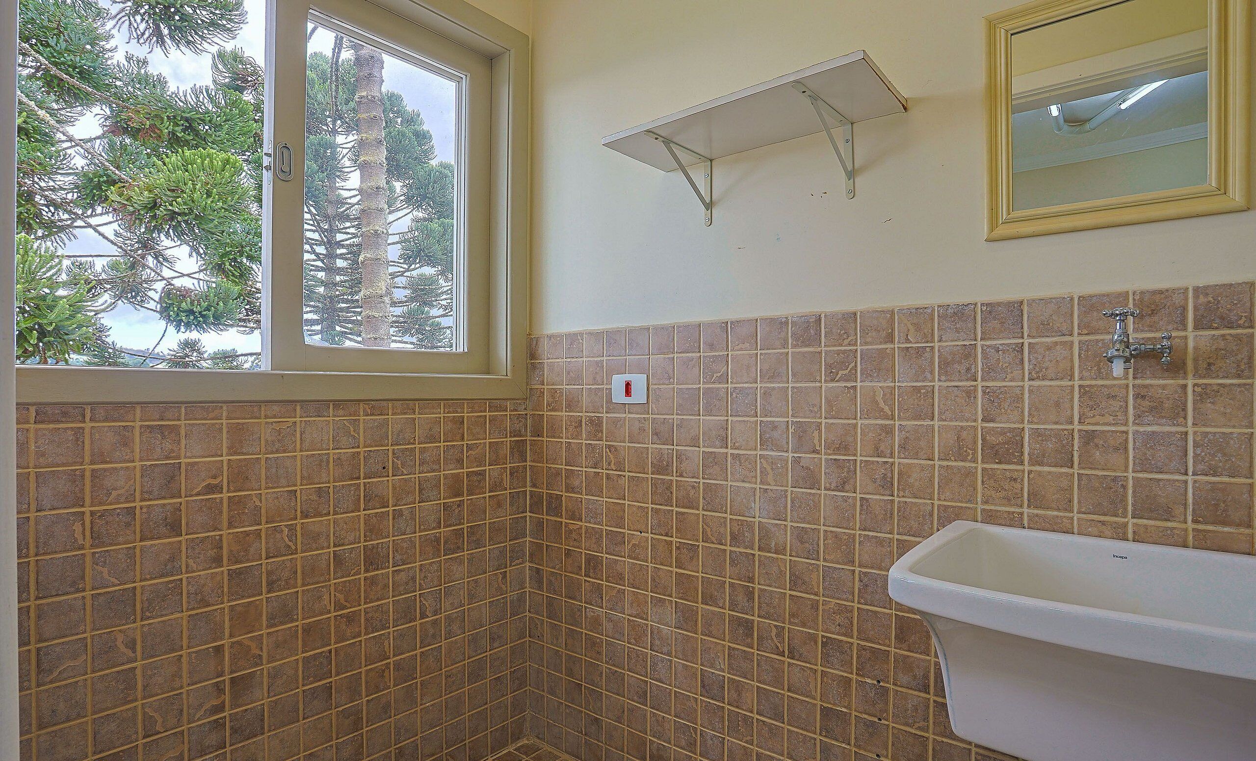 Ein Badezimmer mit Fenster, gefliesten Wänden, einem Waschbecken und einem Spiegel.