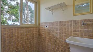 Ein Badezimmer mit Fenster, gefliesten Wänden, einem Waschbecken und einem Spiegel.