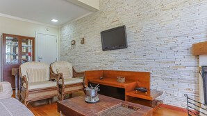 A living room with a stone wall, a flat-screen TV, wicker furniture, and a wooden table. - Apart w Beautiful View in Campos do Jordao Lvr0003 (Campos do Jordão)
