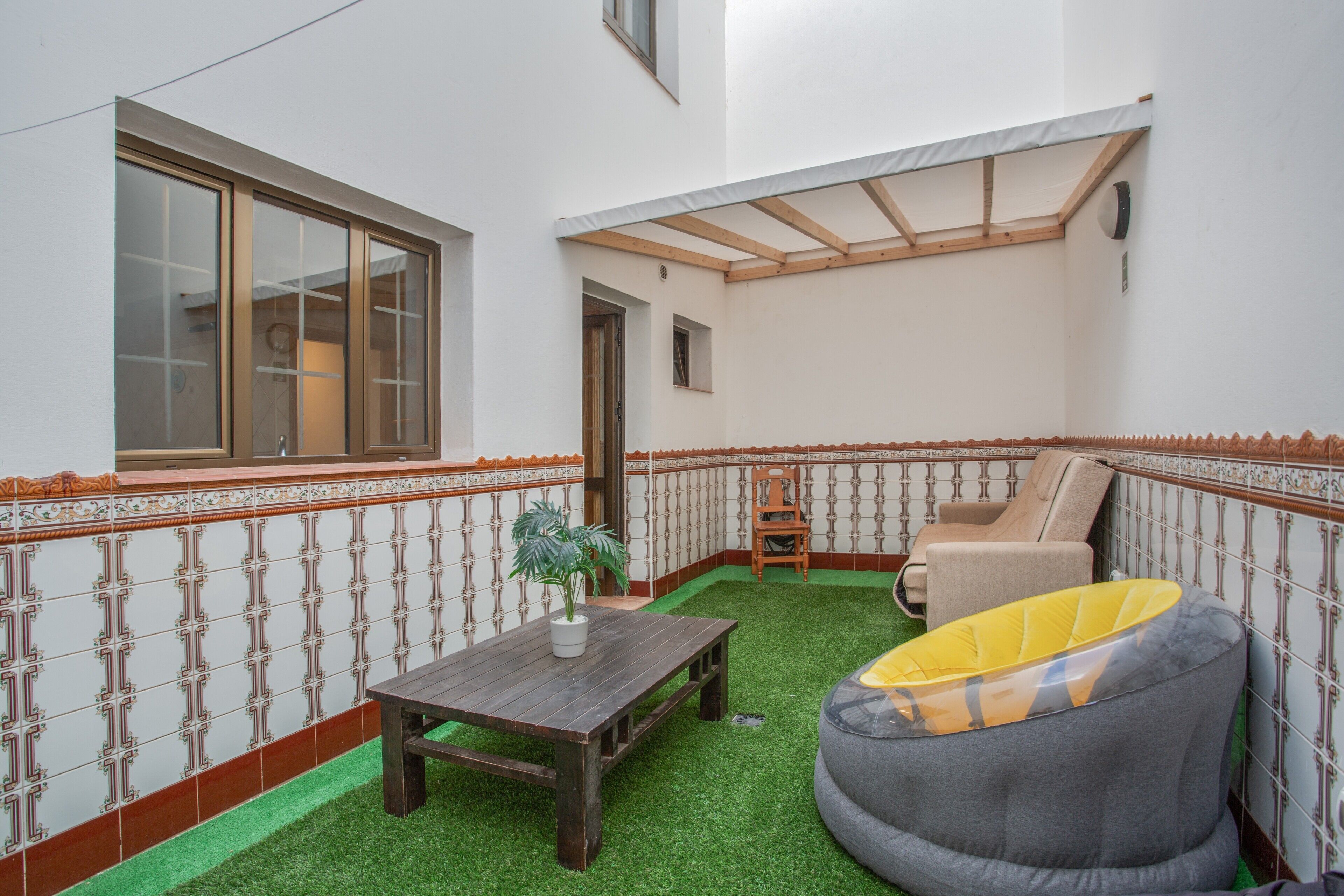 Une pièce avec un banc en bois, une plante en pot, un pouf jaune et une fenêtre donnant sur un beau paysage.