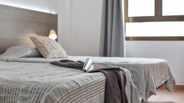 Ein Schlafzimmer mit zwei Betten, einer Nachttischlampe und einem Fenster mit Vorhängen.