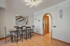 Un comedor con mesa de vidrio, sillas de metal, lámpara de techo, puerta de madera y un atrapasueños en la pared.