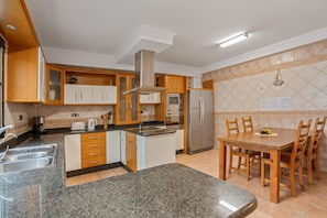 Una cocina con encimeras de granito, armarios de madera, un refrigerador de acero inoxidable y una mesa de comedor con sillas.