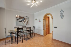 A dining area with a glass table, metal chairs, a ceiling light fixture, a wooden door, and a dreamcatcher on the wall.