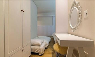 Quarto com cama, guarda-roupa, penteadeira com espelho e um banquinho macio.