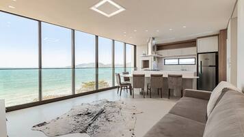 A modern kitchen with large windows overlooking a body of water, a dining area with chairs, and a large rug on the floor.