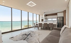 Una cocina moderna con amplios ventanales que dan a una extensión de agua, un comedor con sillas y una alfombra grande en el suelo.