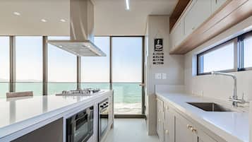 A modern kitchen with a large island, built-in oven, and a view of the sea.