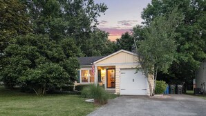 A single-story house with a garage, surrounded by trees and a well-maintained lawn. - Charming Cottage - Near I-75 & Horse Park + Farms (Lexington)