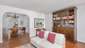 A living room with a white sofa, wooden cabinet, dining table, and chairs. - Charming Cottage - Near I-75 & Horse Park + Farms (Lexington)
