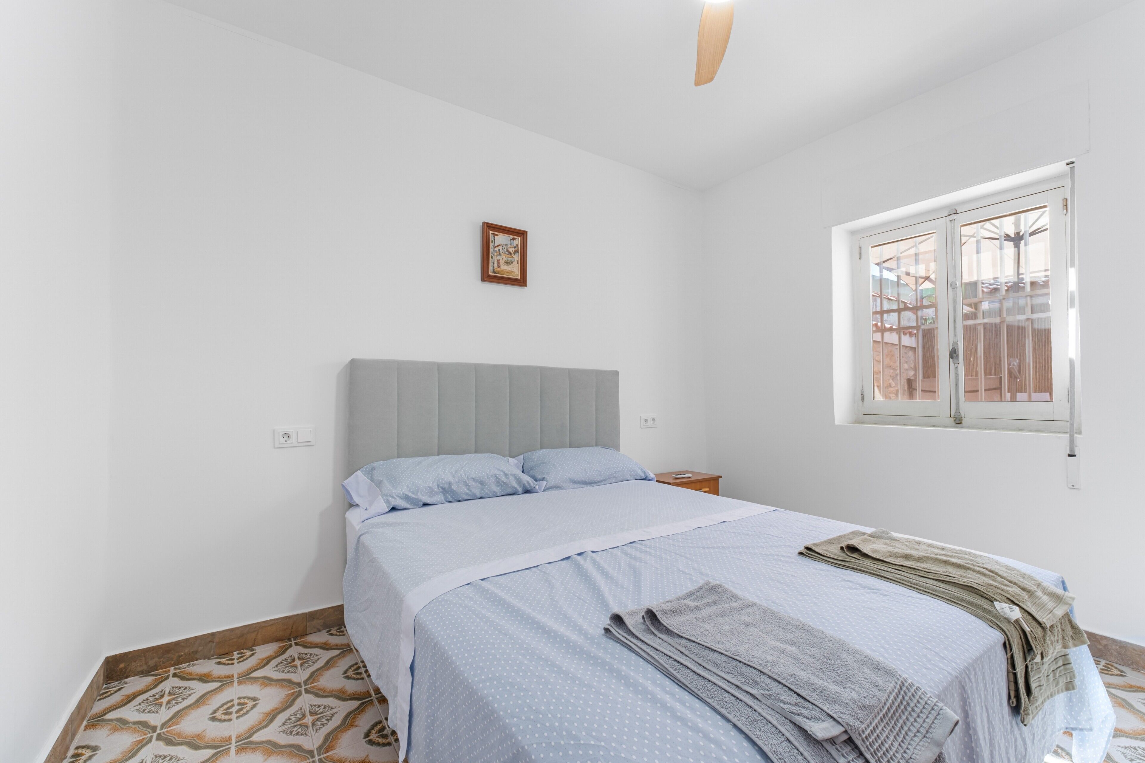 Une chambre à coucher avec un lit, une fenêtre, un tableau accroché au mur et un sol à motifs.