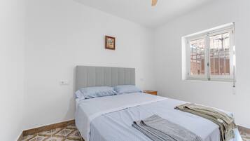 Une chambre à coucher avec un lit, une fenêtre, un tableau accroché au mur et un sol à motifs.