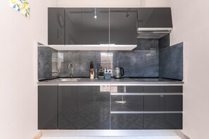 Una cocina moderna con armarios oscuros, un lavamanos de acero inoxidable y una campana extractora integrada.