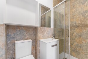 A bathroom with a toilet, sink, and glass shower enclosure.