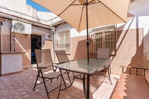 An outdoor patio with a glass table and chairs, an umbrella, and patterned tiles.