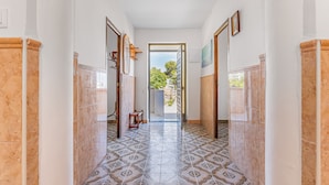 A hallway with patterned floor tiles, white walls, and a door leading outside.