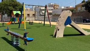 A playground with various play equipment, including swings and a seesaw, set on artificial grass.