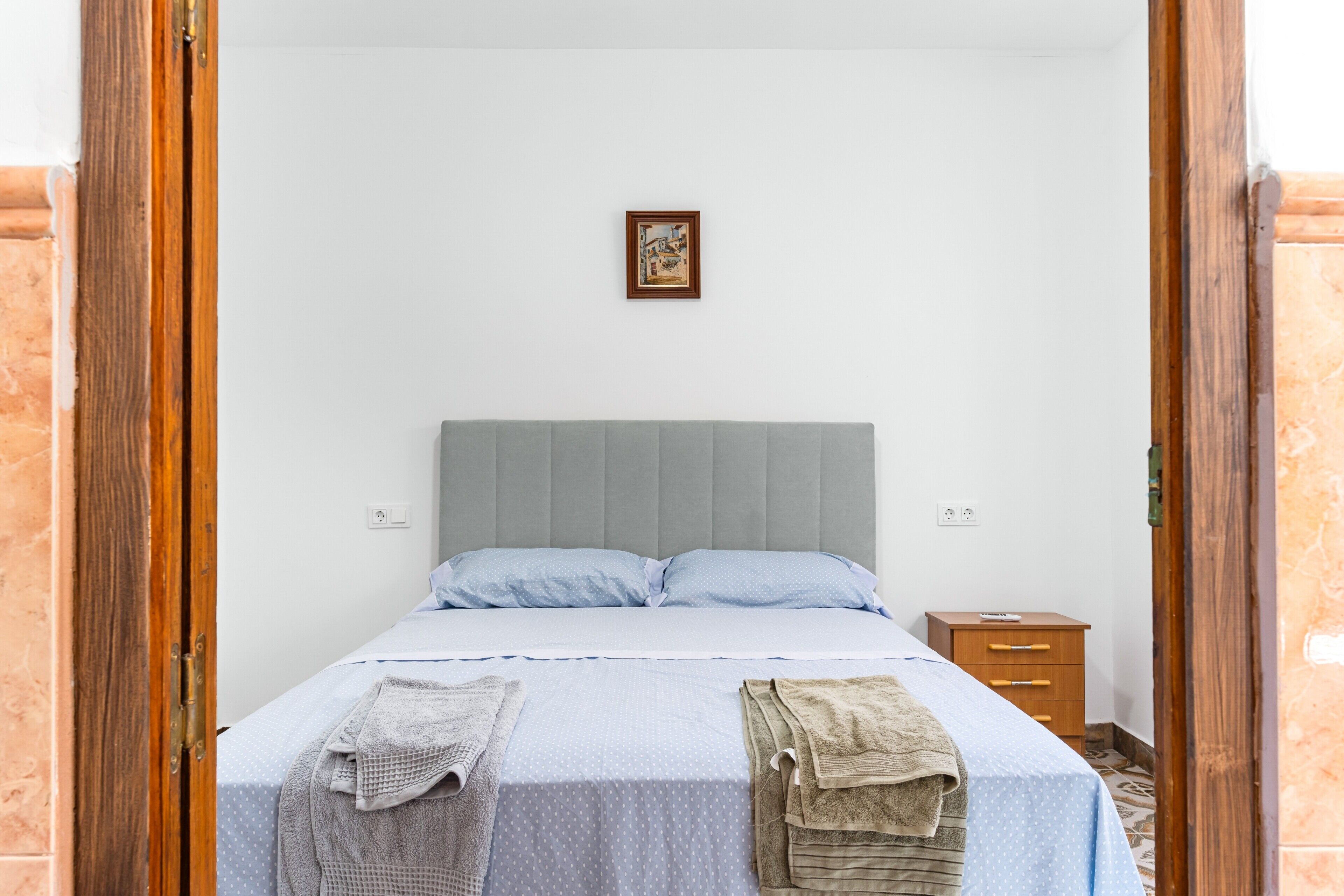A bedroom with a bed, a nightstand, and a framed picture on the wall.