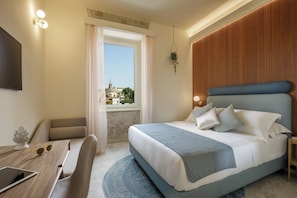 A modern hotel room with a large bed, a desk with a tablet, a chair, a TV, and a view of a cityscape through a window. - Rome for Two (Rome)