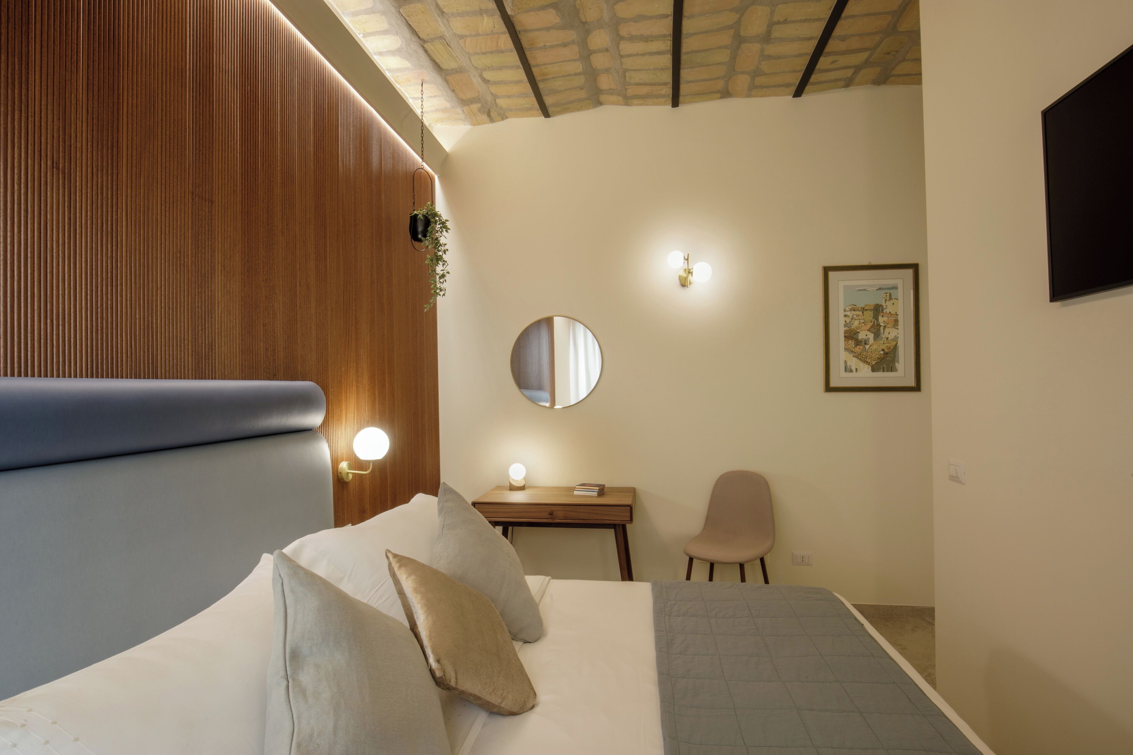A modern bedroom with a bed, bedside table, mirror, and a desk with a chair.