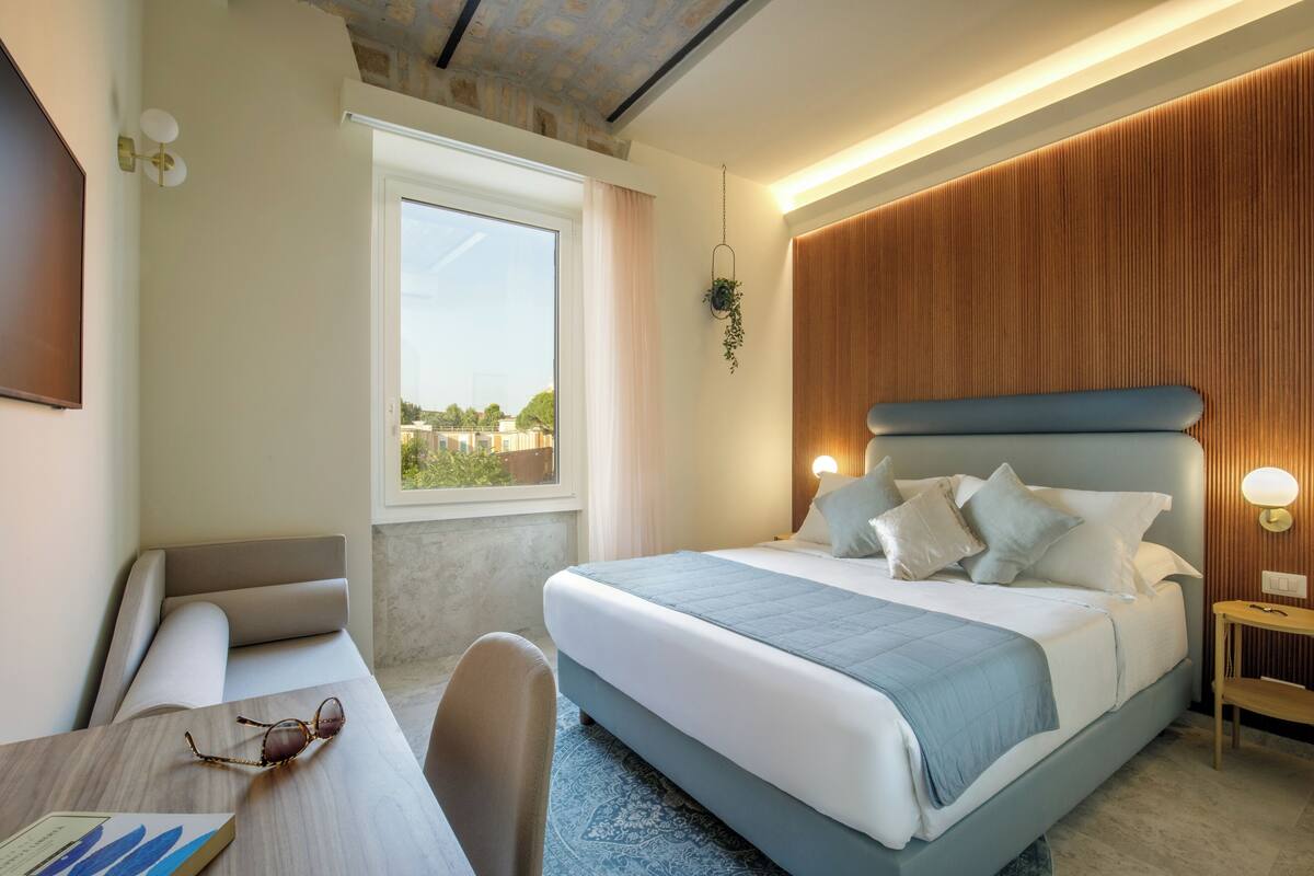 Ein modernes Hotelzimmer mit einem großen Bett, einem Schreibtisch mit Stuhl, einem Fenster mit Blick und einer Wand mit Holzverkleidung.