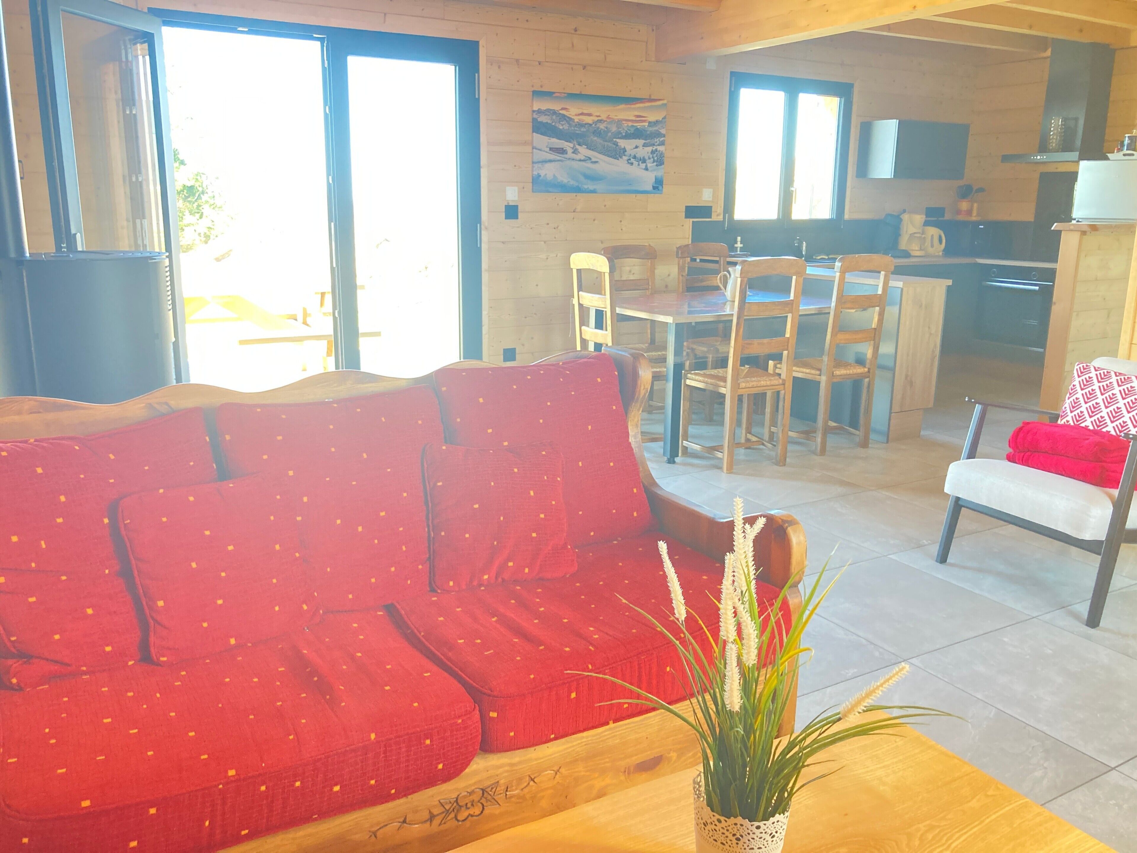 A cozy living room with a red sofa, a wooden dining table, and a kitchen area in the background.
