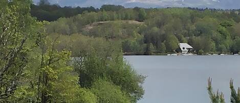 A lake with a house on the shore, surrounded by trees and mountains in the background.