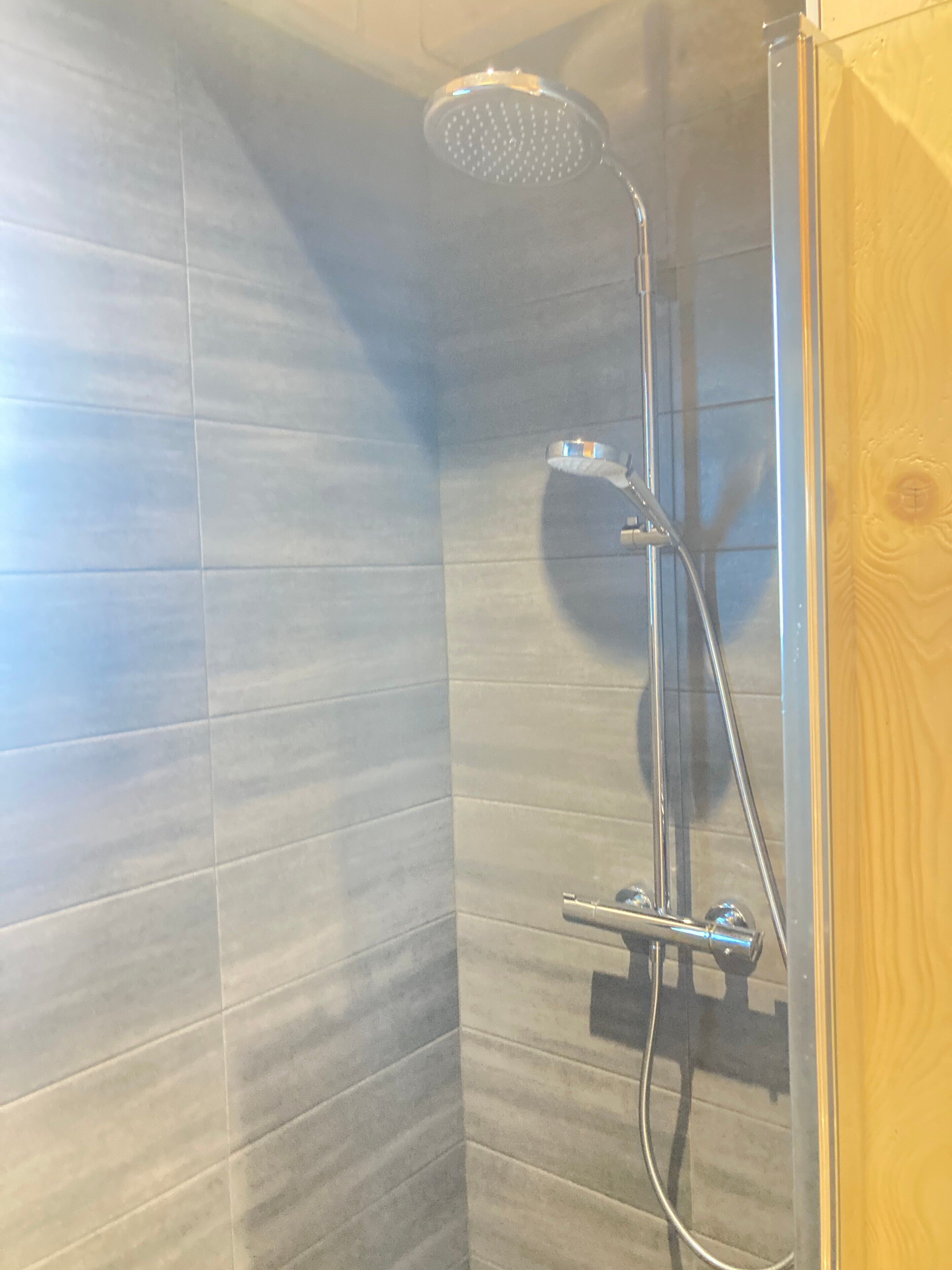 A shower with a handheld showerhead and a wall-mounted faucet.