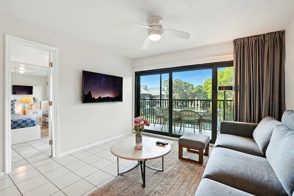 A modern living room with a large window, a ceiling fan, and a view of the outdoors.