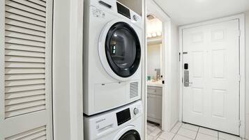 A stacked washer and dryer unit in a hallway with a white door and a tiled floor.