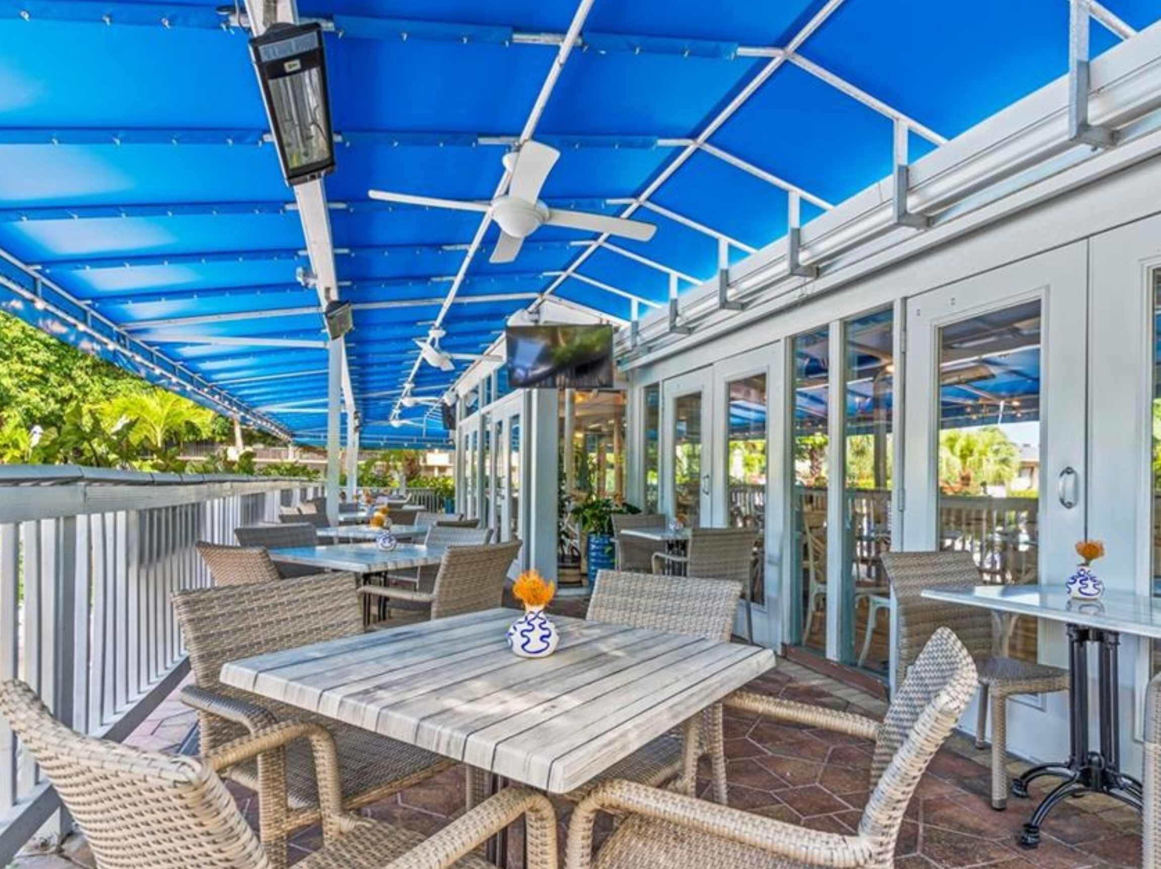 Un patio al aire libre con mesas y sillas, un ventilador de techo y vistas del interior.