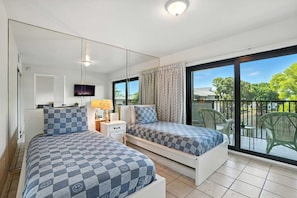 A bedroom with two beds, a TV, a bedside table, and a view of the outdoors.