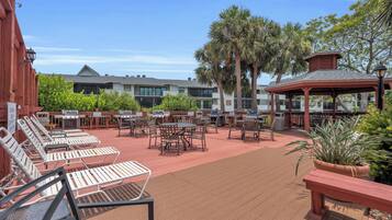An outdoor patio with multiple barbecue grills, lounge chairs, and tables.