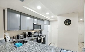 A modern kitchen with grey cabinets, a microwave, a refrigerator, a coffee maker, and a clock on the wall.