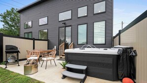 A modern house with a patio area featuring outdoor furniture, a hot tub, and a grill.