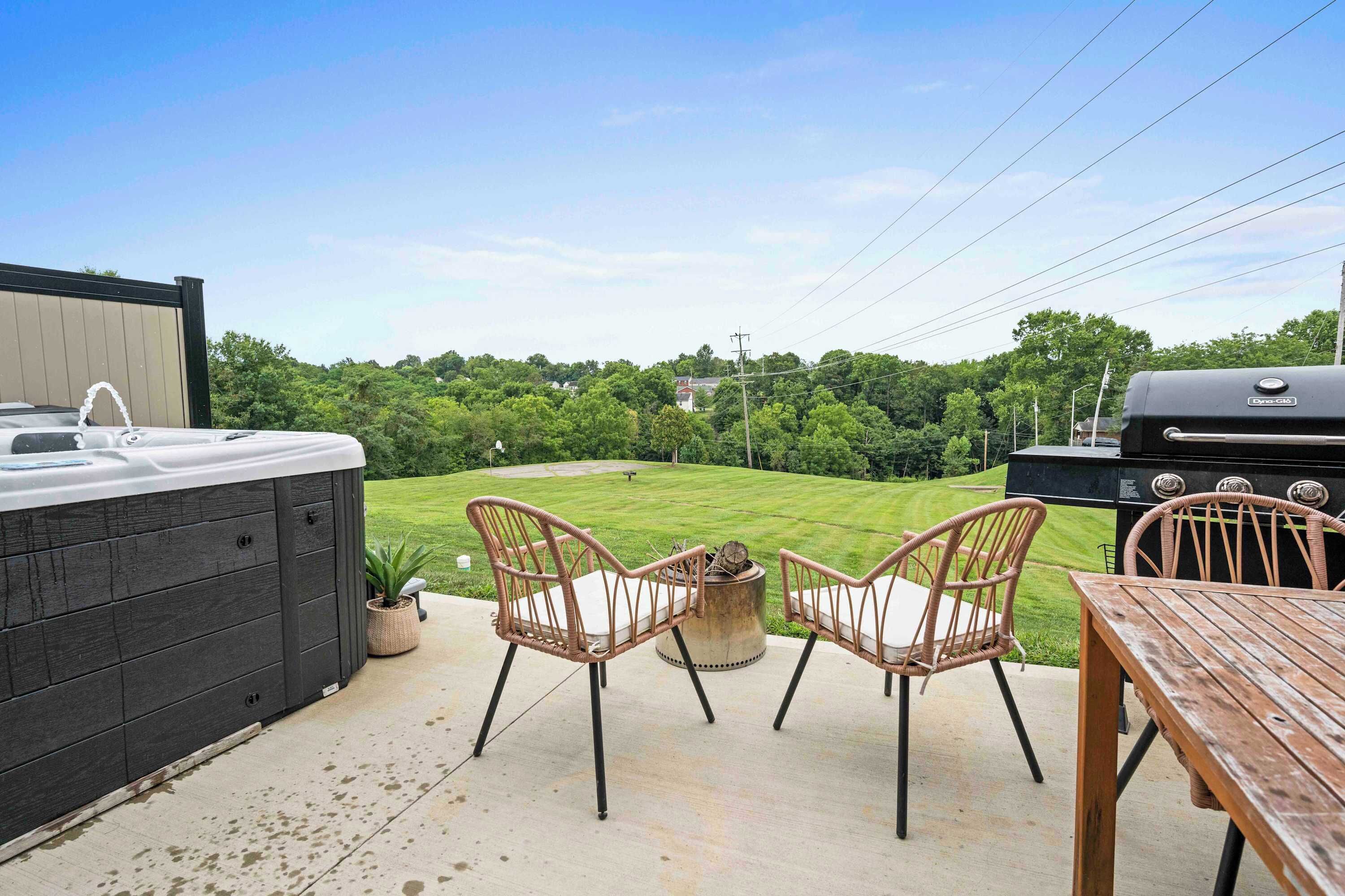 Een terras met een hottub, twee rieten stoelen, een houten tafel en een barbecue.