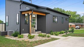 A modern two-story house with a grey exterior, a front porch with wooden beams, and a small garden area with rocks and plants.